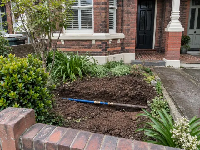 Exposed repaired water pipe in a front garden trench beside a brick house in Randwick