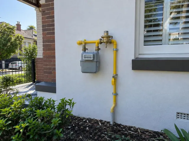 Exterior gas meter and yellow pipework on a white wall beside a window in Kensington